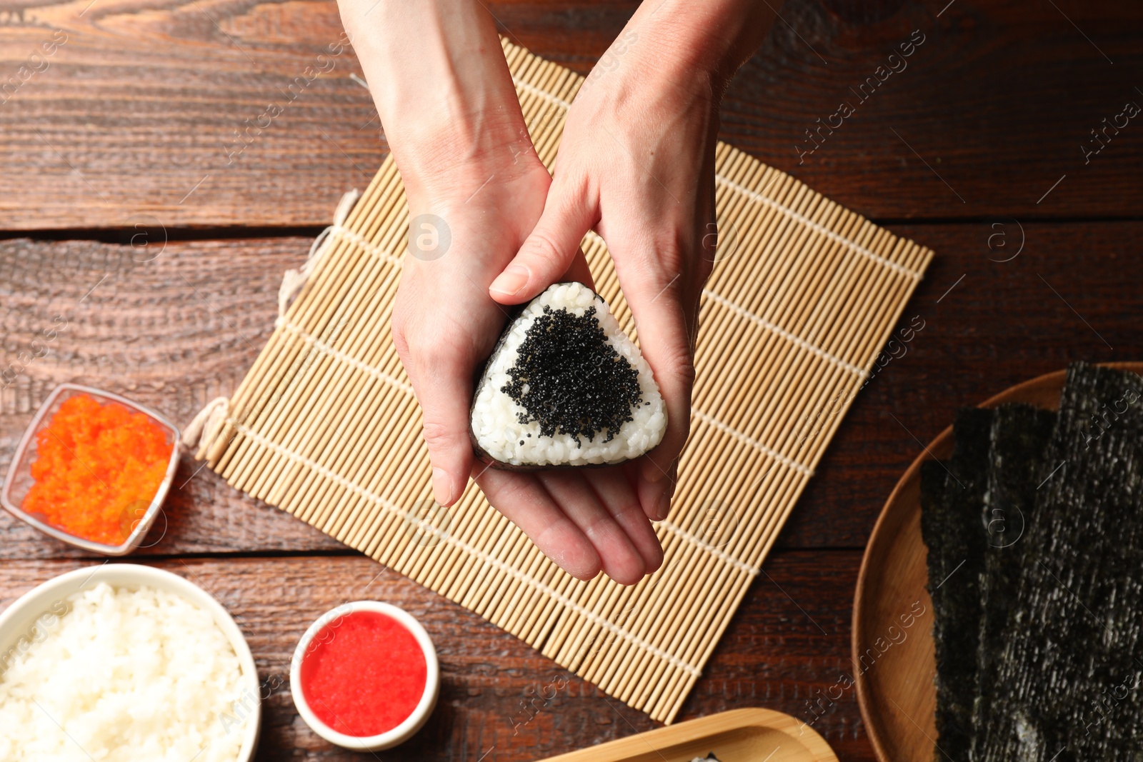 Photo of Woman with tasty tobiko onigiri (Japanese rice ball) at wooden table, top view