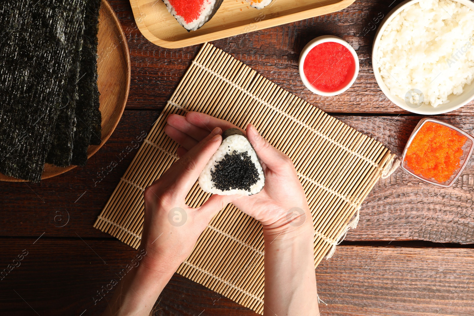 Photo of Woman with tasty tobiko onigiri (Japanese rice balls) at wooden table, top view