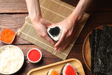 Photo of Woman with tasty tobiko onigiri (Japanese rice balls) at wooden table, top view