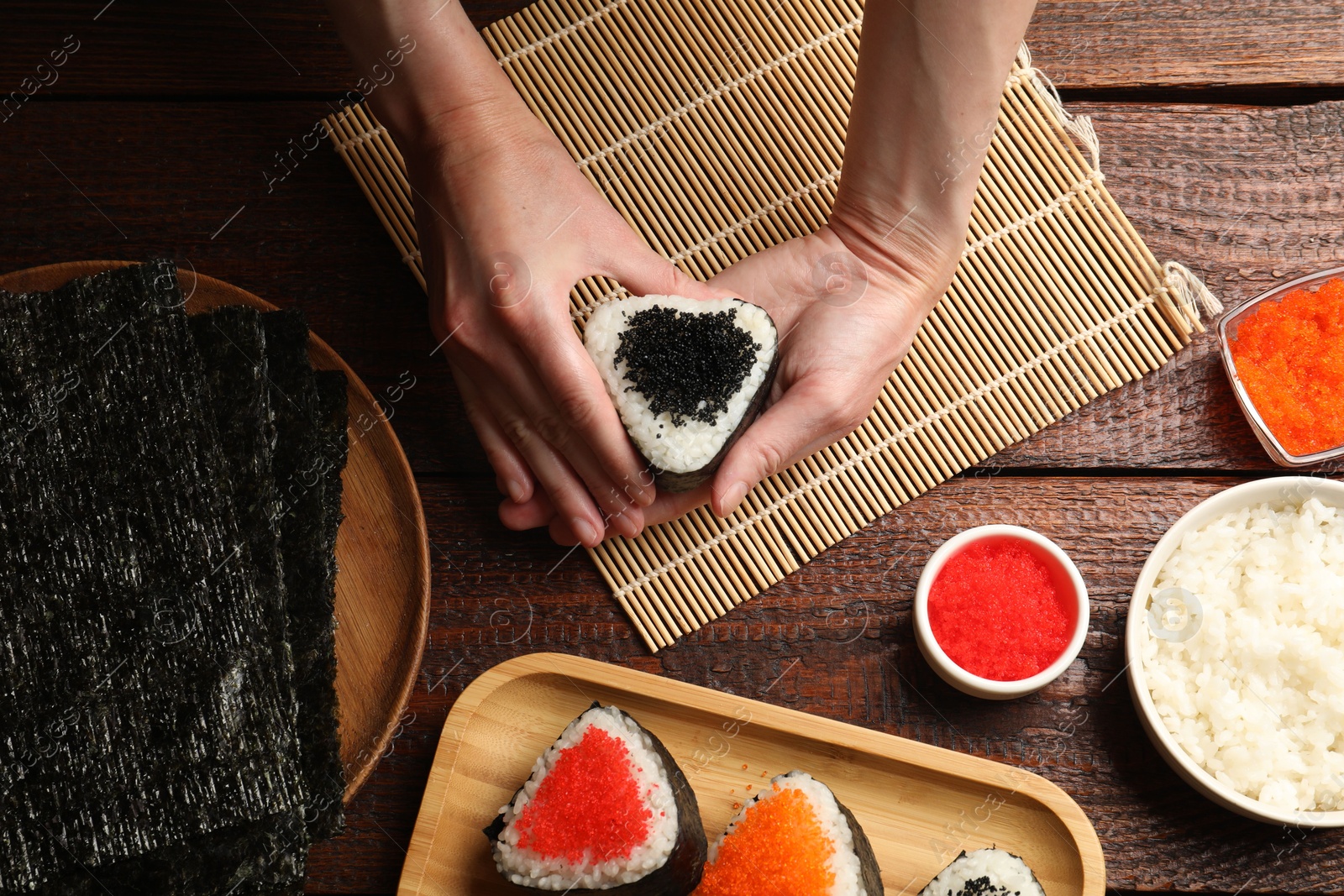 Photo of Woman with tasty tobiko onigiri (Japanese rice balls) at wooden table, top view