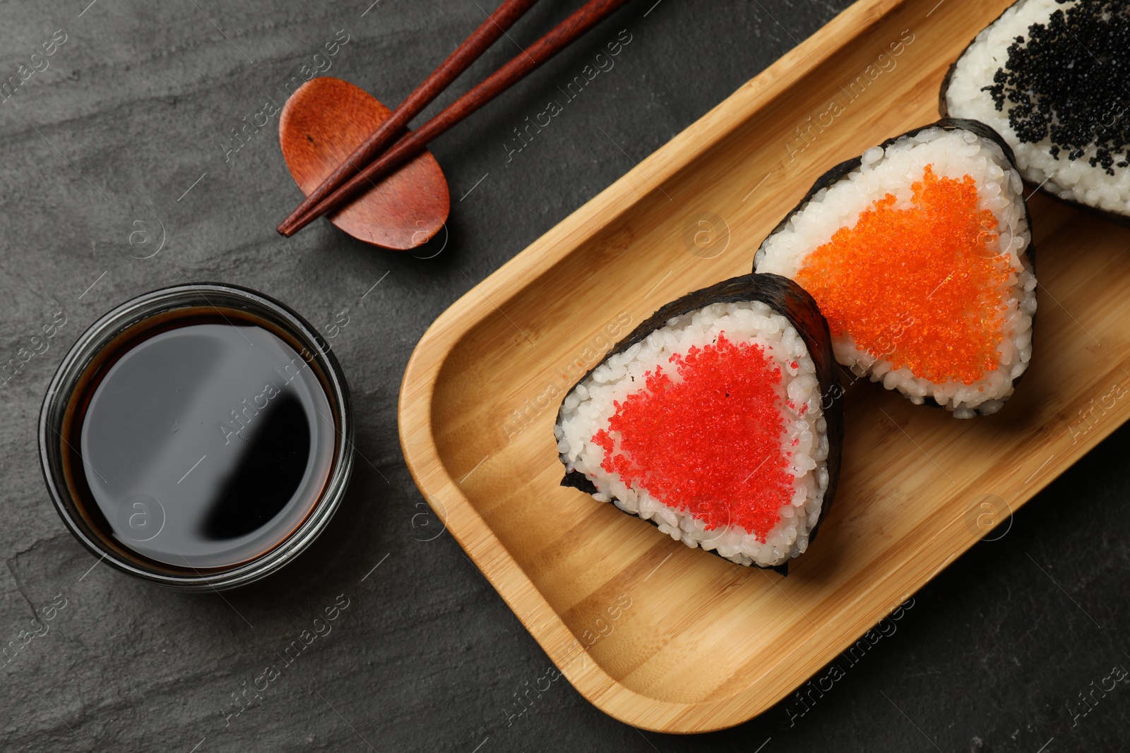 Photo of Tasty tobiko onigiri (Japanese rice balls) served on black table, flat lay