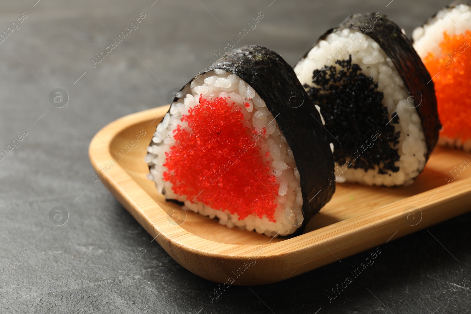 Photo of Tasty tobiko onigiri (Japanese rice balls) on black table, closeup