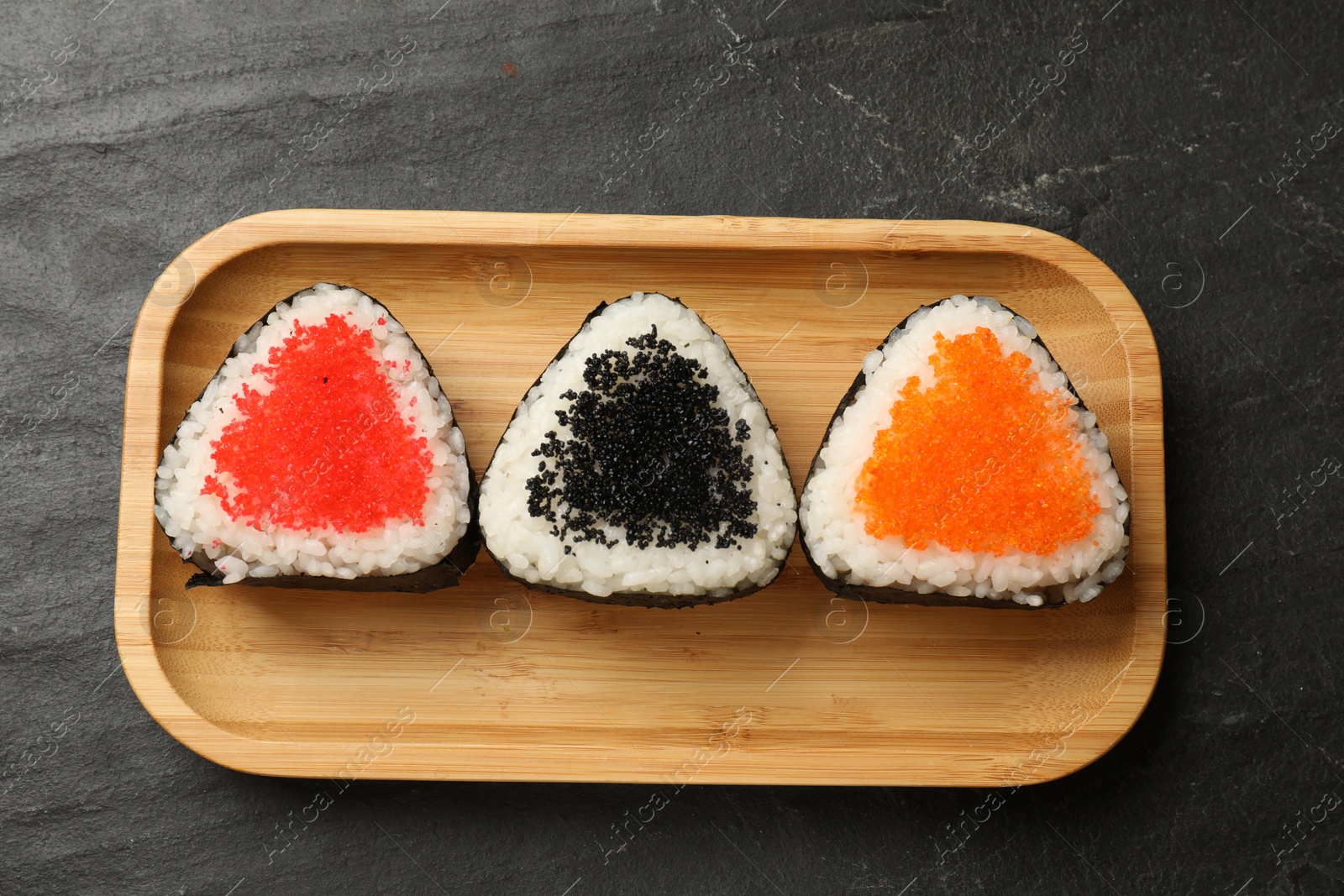 Photo of Tasty tobiko onigiri (Japanese rice balls) on black table, top view