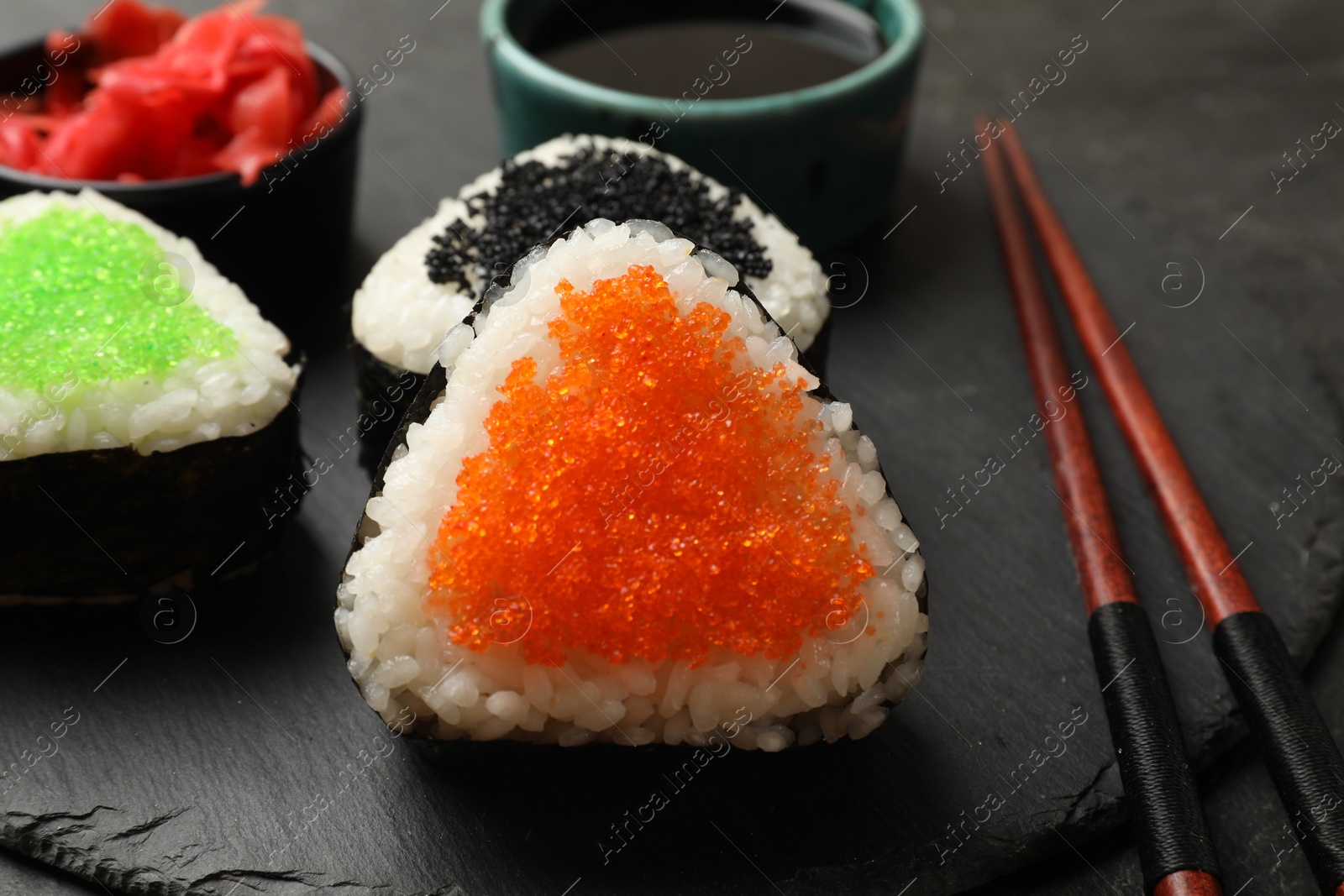 Photo of Tasty tobiko onigiri (Japanese rice balls) served on black table, closeup