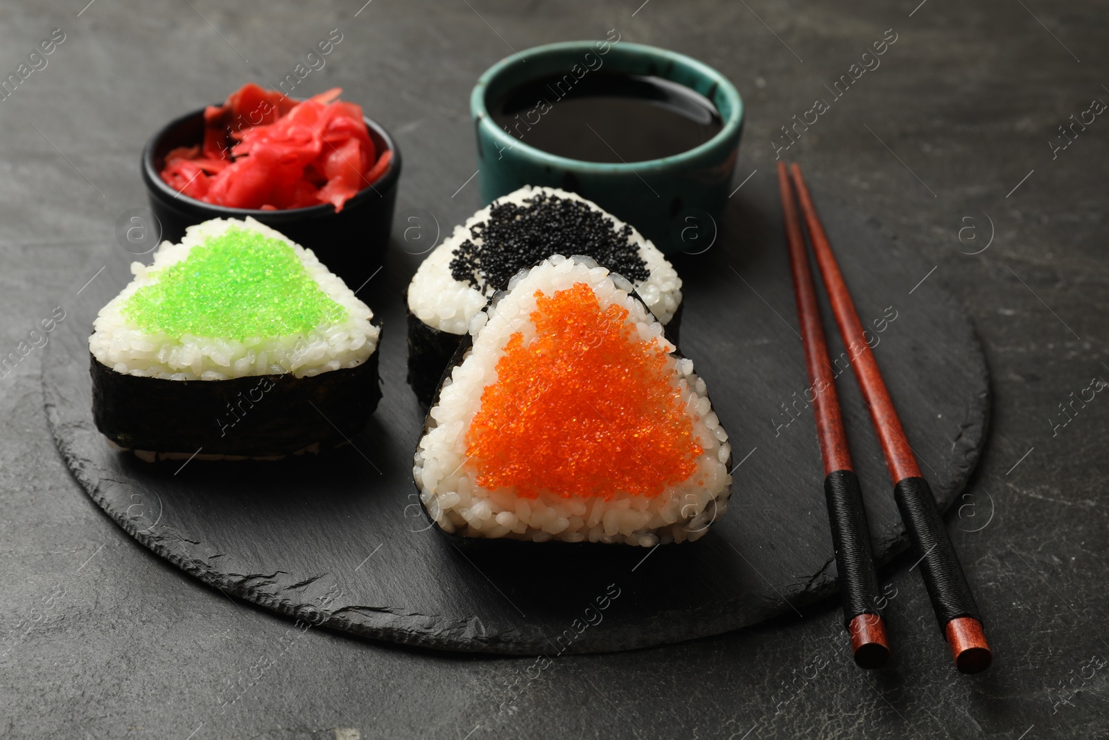 Photo of Tasty tobiko onigiri (Japanese rice balls) served on black table, closeup