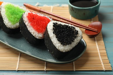 Photo of Tasty tobiko onigiri (Japanese rice balls) served on light blue wooden table, closeup