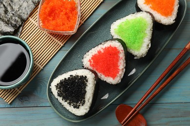 Photo of Tasty tobiko onigiri (Japanese rice balls) served on light blue wooden table, flat lay