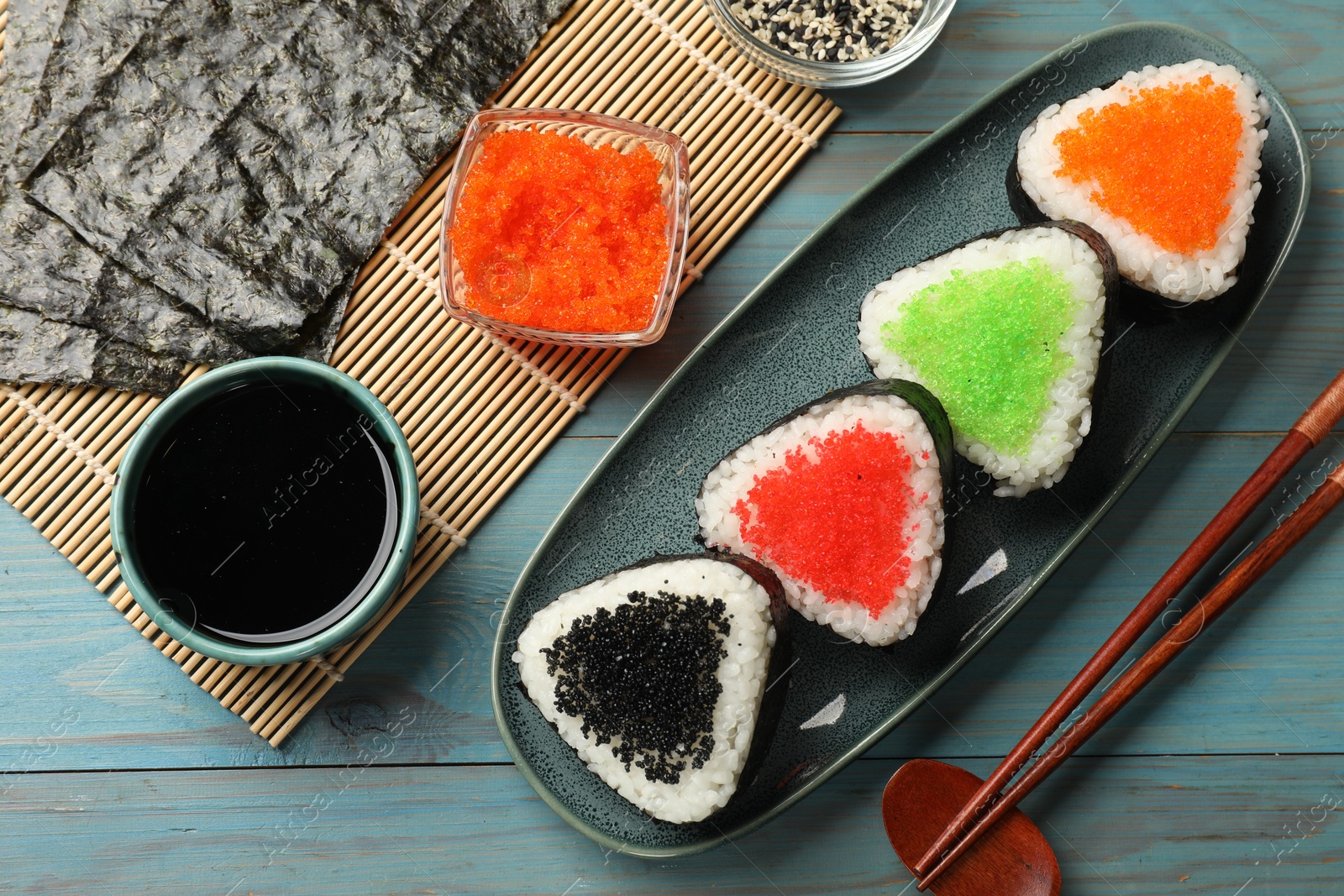 Photo of Tasty tobiko onigiri (Japanese rice balls) served on light blue wooden table, flat lay