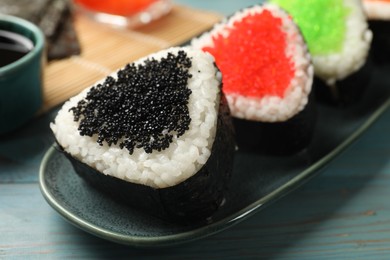 Photo of Tasty tobiko onigiri (Japanese rice balls) on light blue wooden table, closeup