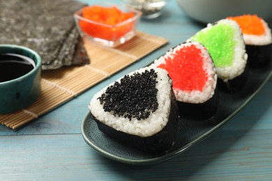 Photo of Tasty tobiko onigiri (Japanese rice balls) served on light blue wooden table, closeup