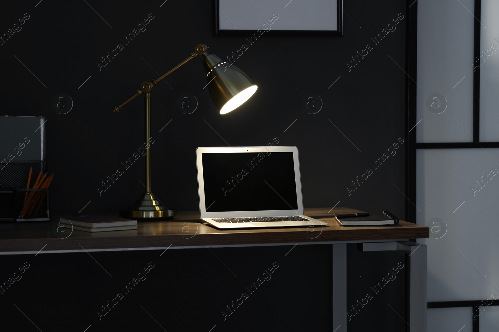 Comfortable workplace with laptop and lamp on wooden desk at home office in evening Photo of Comfortable workplace with laptop and lamp on wooden desk at home office in evening