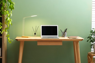 Photo of Home office. Comfortable workplace near light green wall. Desk with laptop and lamp in room