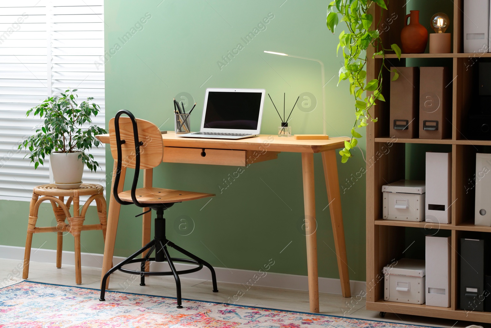 Home office. Comfortable workplace with laptop and stationery on wooden desk in room Photo of Home office. Comfortable workplace with laptop and stationery on wooden desk in room