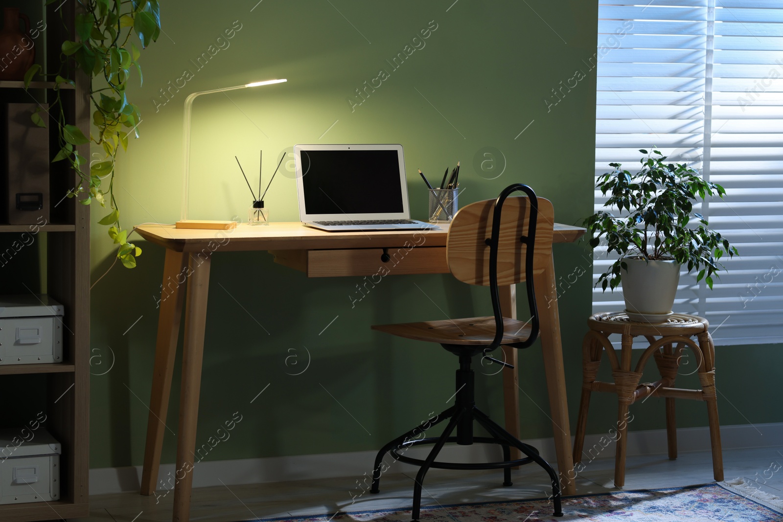 Comfortable workplace with laptop and lamp on wooden desk at home office in evening Photo of Comfortable workplace with laptop and lamp on wooden desk at home office in evening