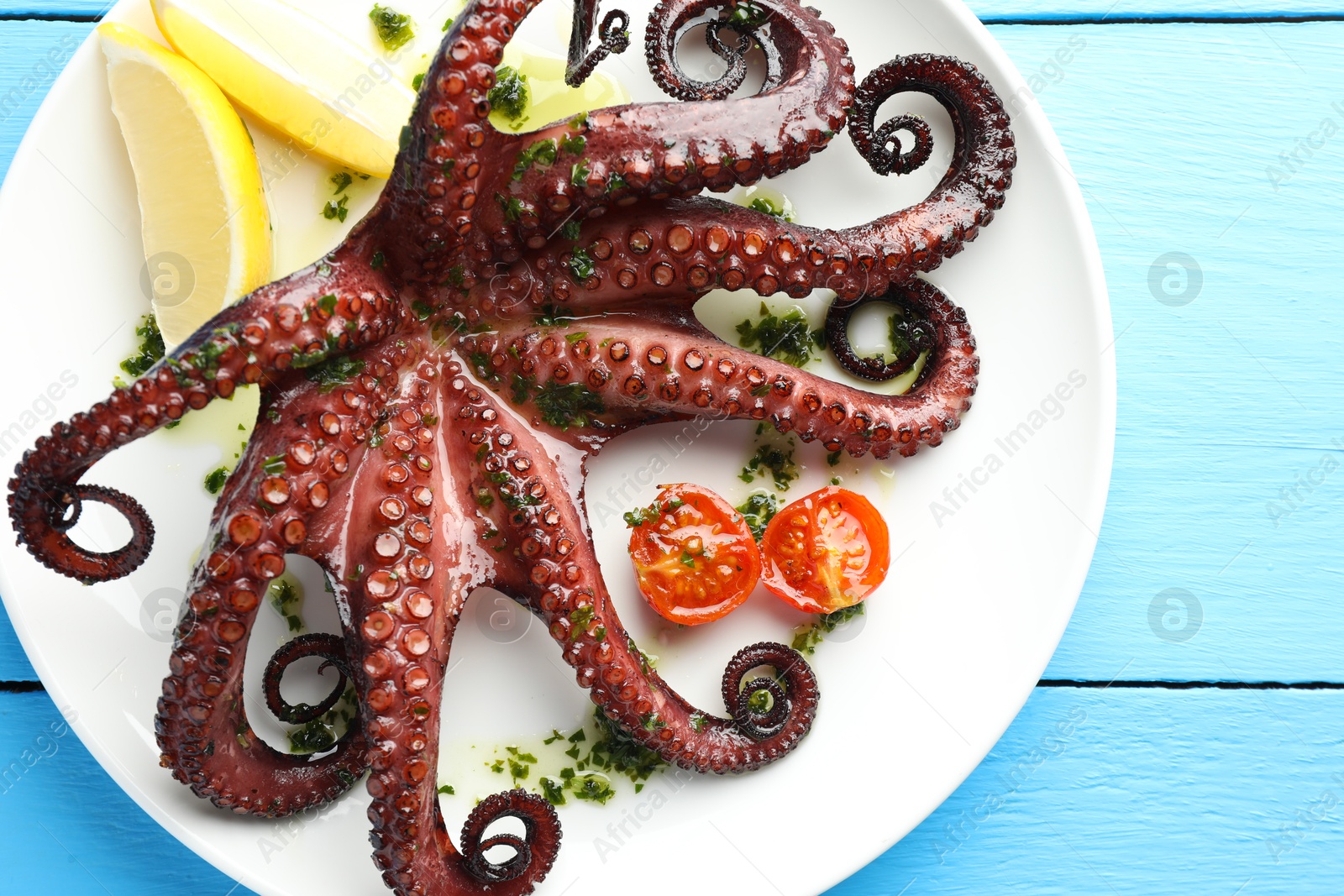 Photo of Fried octopus with herb sauce, lemon and tomatoes on light blue wooden table, top view