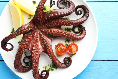 Fried octopus with herb sauce, lemon and tomatoes on light blue wooden table, top view