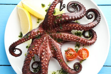 Photo of Fried octopus with herb sauce, lemon and tomatoes on light blue wooden table, top view