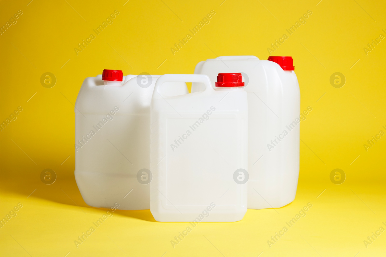 Photo of Three plastic canisters with caps on yellow background