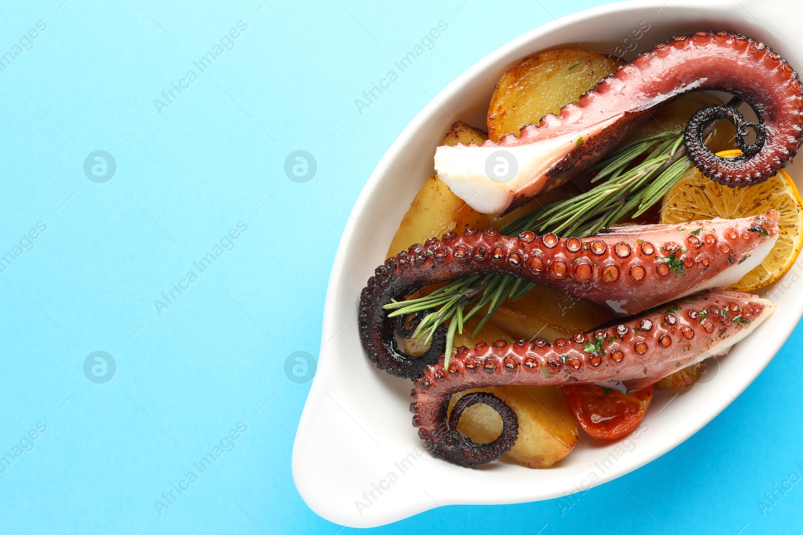 Photo of Fried octopus with vegetables, lemon and rosemary in baking dish on light blue background, top view. Space for text