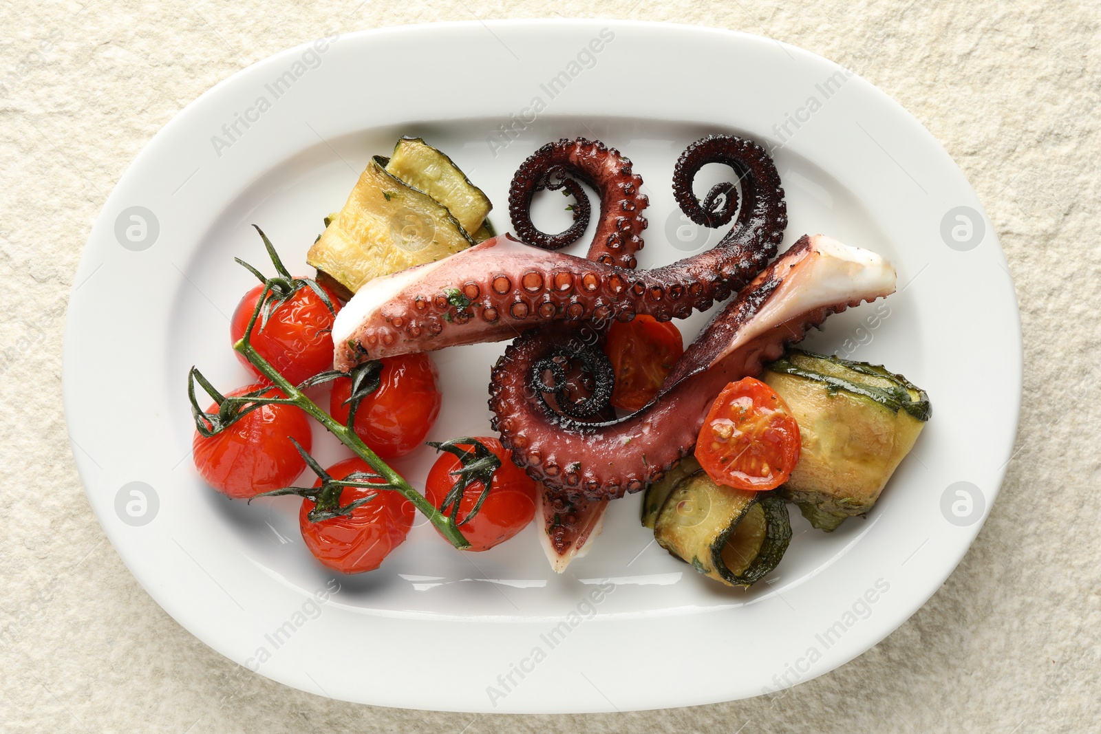 Photo of Fried octopus with zucchini and tomatoes on light textured table, top view