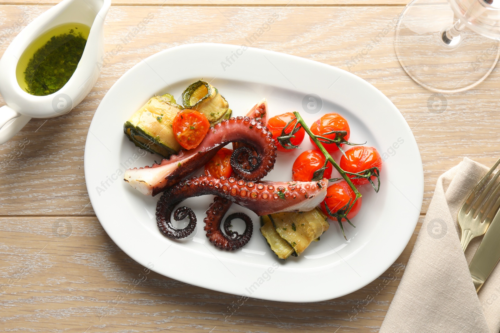 Photo of Fried octopus with herb sauce, zucchini and tomatoes on wooden table, flat lay