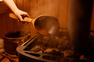 Photo of Woman pouring water on stones in sauna, closeup