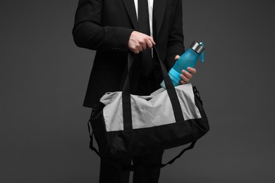 Photo of Man in suit putting bottle of water into gym bag on dark grey background, closeup