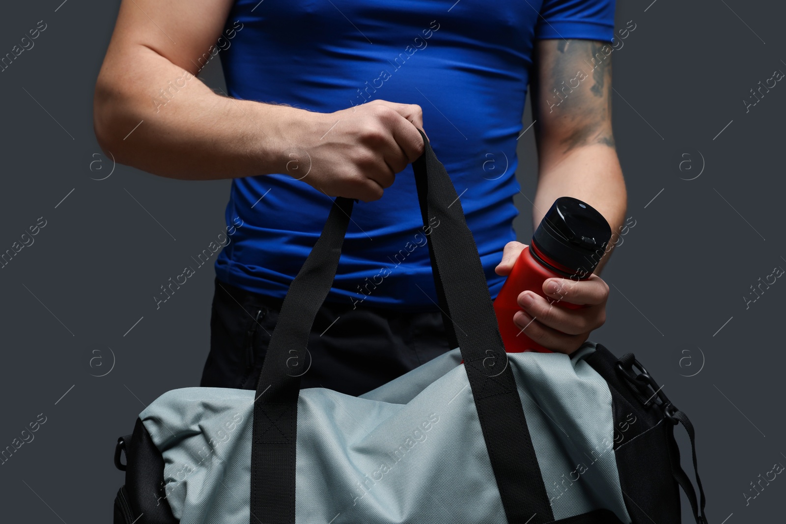 Photo of Man putting bottle of water into gym bag on dark grey background, closeup