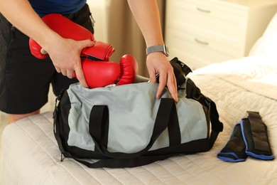 Photo of Man putting boxing gloves into gym bag indoors, closeup