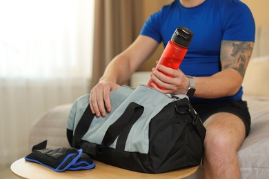 Photo of Man putting bottle of water into gym bag indoors, closeup