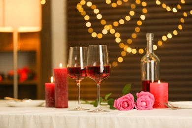 Photo of Romantic table setting with red wine, burning candles and roses in restaurant