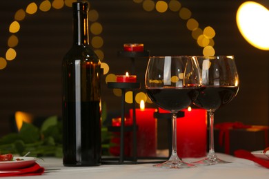 Photo of Romantic table setting with red wine and burning candles against blurred lights