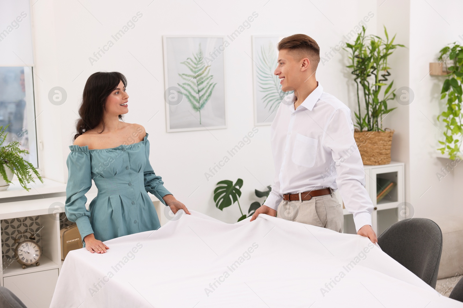 Photo of Couple putting white tablecloth on table at home