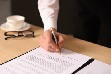 Photo of Man putting signature on document at wooden table, closeup