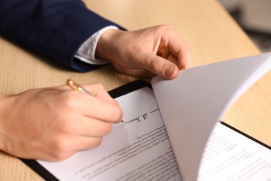 Photo of Man putting signature on document at wooden table, closeup