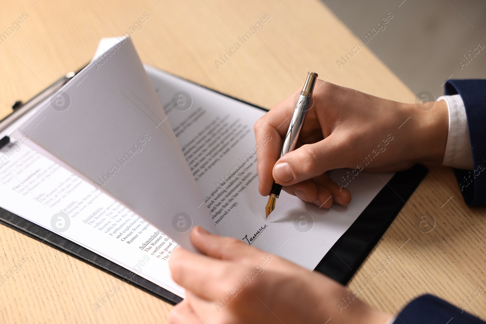 Photo of Man putting signature on document at wooden table, closeup