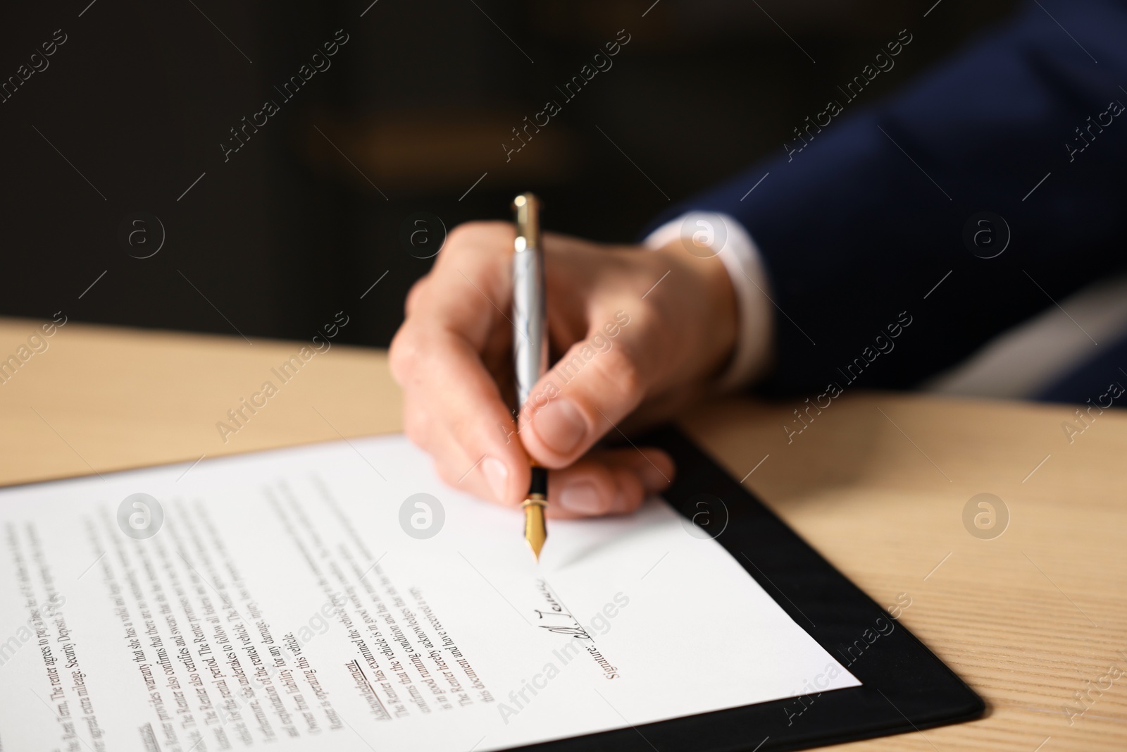 Photo of Man putting signature on document at wooden table, closeup