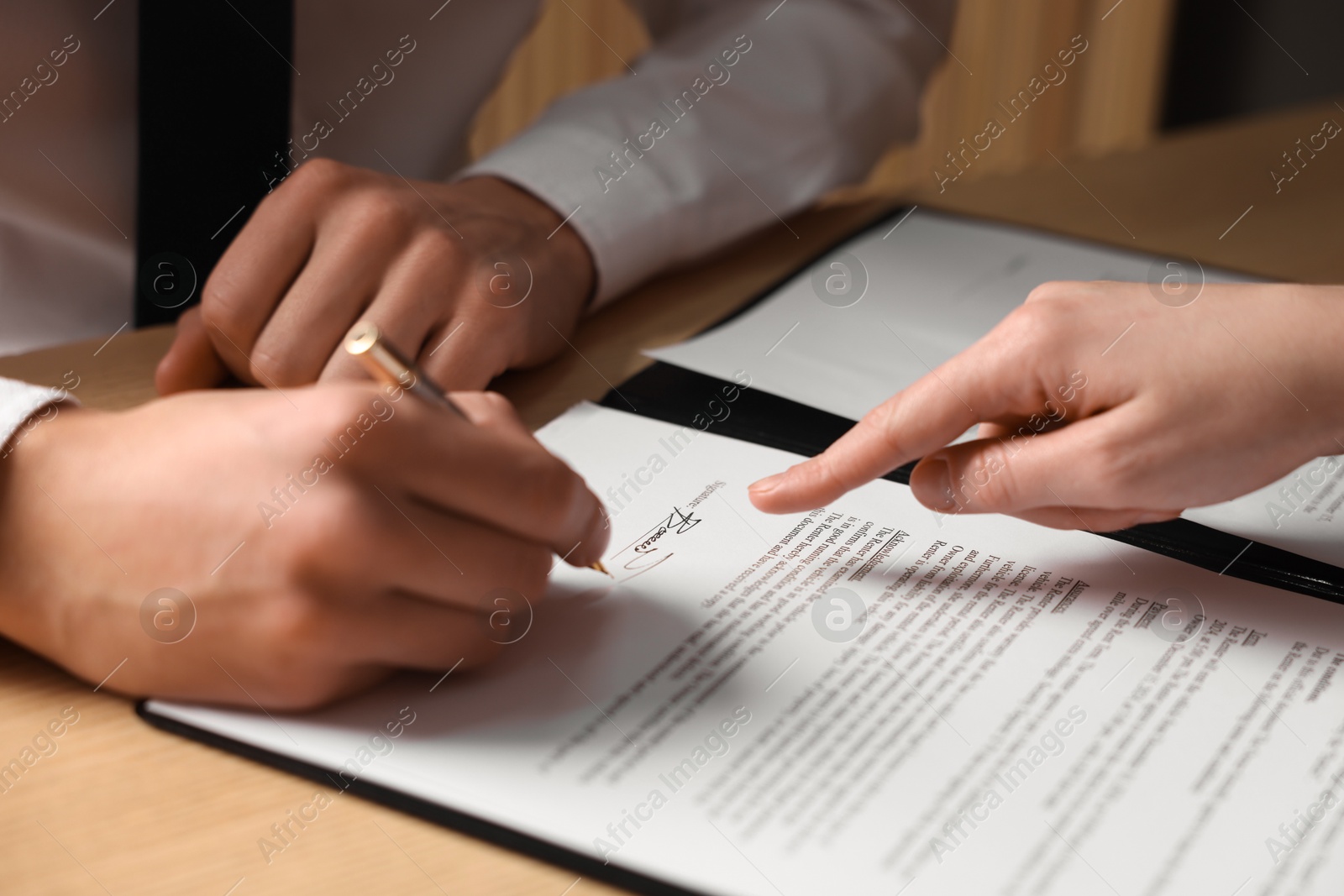 Photo of Woman pointing at document and man putting signature at table, closeup