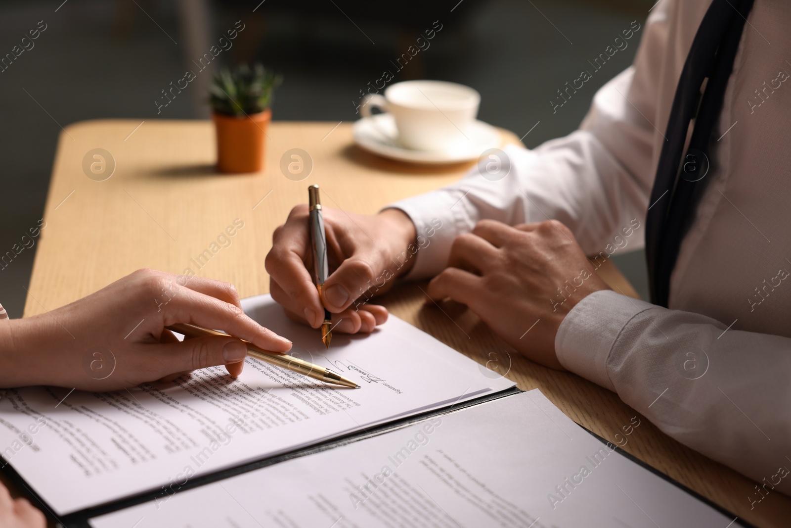 Photo of Woman pointing at document and man putting signature at wooden table, closeup