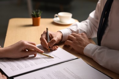 Photo of Woman pointing at document and man putting signature at wooden table, closeup