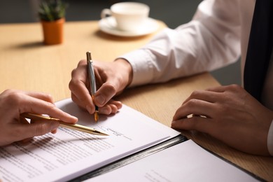 Photo of Woman pointing at document and man putting signature at wooden table, closeup