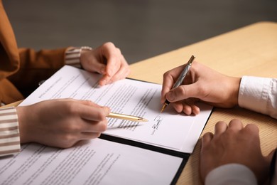 Photo of Woman pointing at document and man putting signature at wooden table, closeup