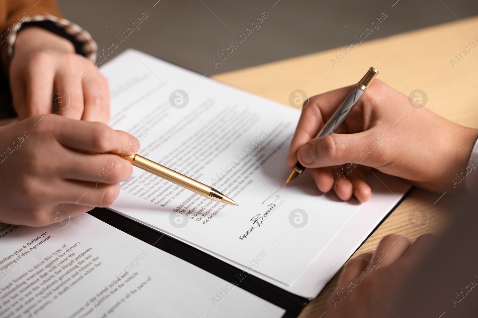 Photo of Woman pointing at document and man putting signature at table, closeup