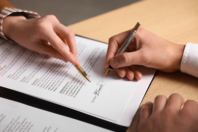 Photo of Woman pointing at document and man putting signature at wooden table, closeup