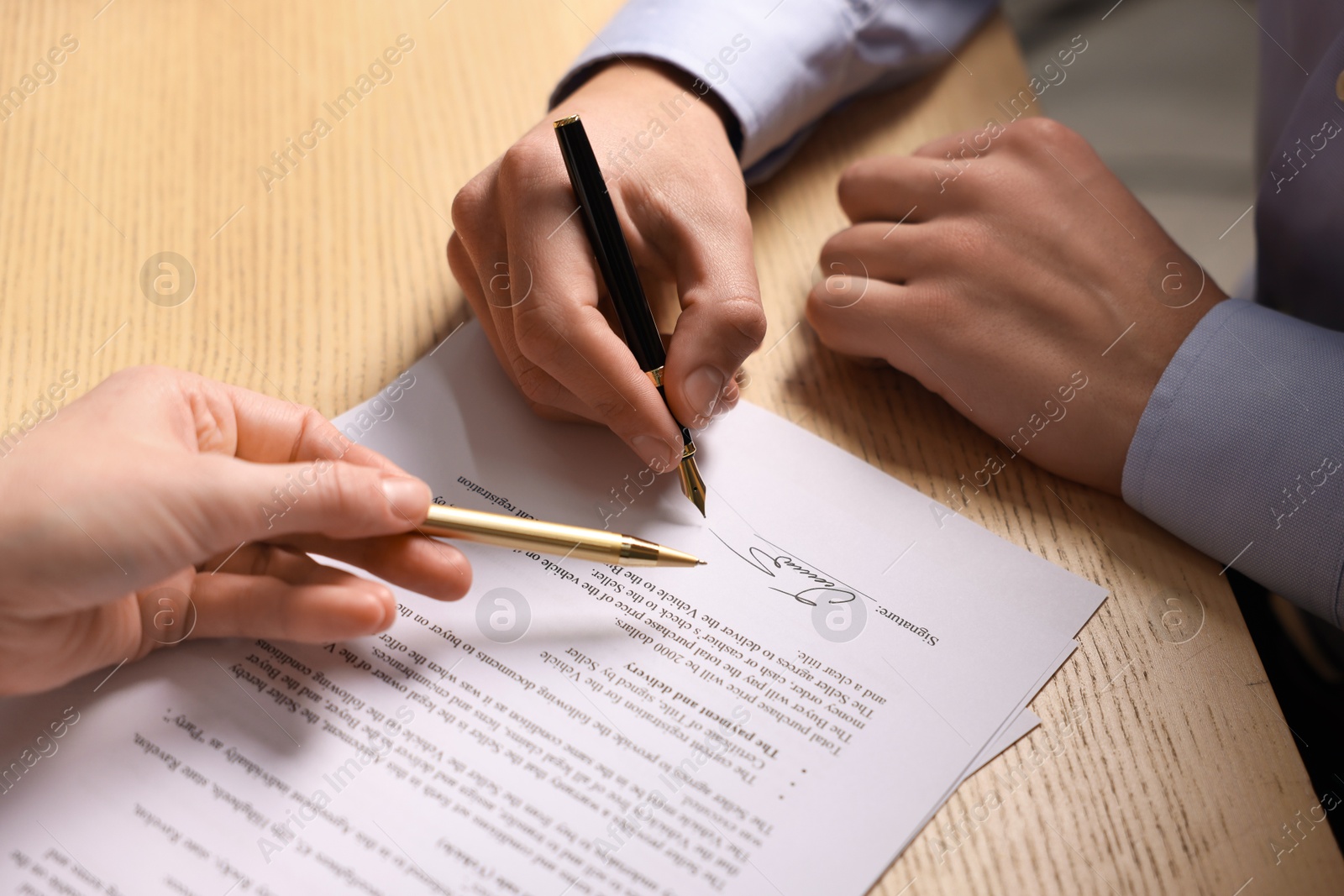 Photo of Woman pointing at document and man putting signature at wooden table, closeup