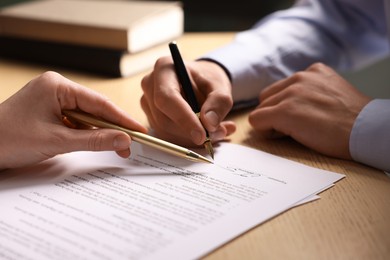 Photo of Woman pointing at document and man putting signature at wooden table, closeup