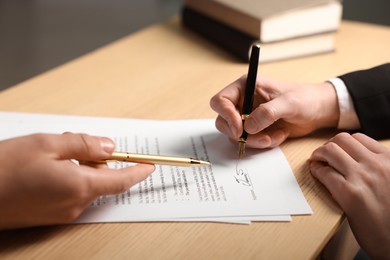 Photo of Man pointing at document and woman putting signature at wooden table, closeup