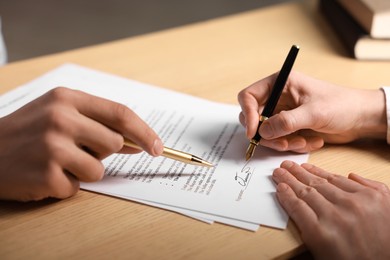 Photo of Man pointing at document and woman putting signature at wooden table, closeup