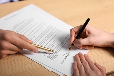 Photo of Man pointing at document and woman putting signature at wooden table, closeup