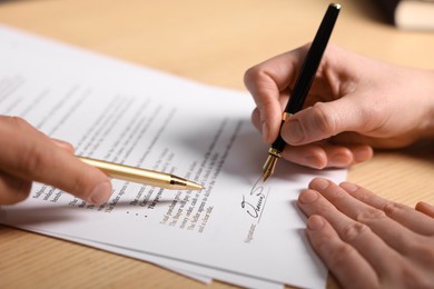 Photo of Man pointing at document and woman putting signature at table, closeup